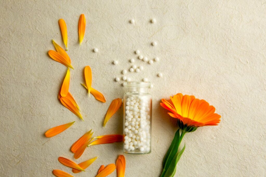 Globuli in einem Glasgefäss mit Ringelblume und Blütenblättern